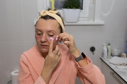 American mom doing postpartum nighttime skincare routine in soft bathroom lighting